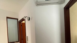 A hallway with a white wall, a door with a frosted glass panel, and a ceiling-mounted air conditioning unit.