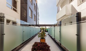 A corridor with glass walls, a central planter with plants, and a view of a building with a tiled facade. - Full Apartment at Ingleses Beach-sc Gge203 (Florianópolis)