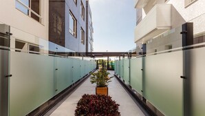 A corridor with glass walls, a central planter with plants, and a view of a building with a tiled facade. - Full Apartment at Ingleses Beach-sc Gge203 (Florianópolis)