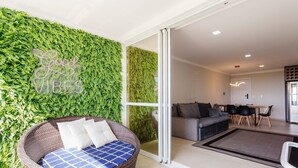 A modern living room with a green wall, a wicker chair with cushions, a grey sofa, and a dining area with a table and chairs. - Full Apartment at Ingleses Beach-sc Gge203 (Florianópolis)