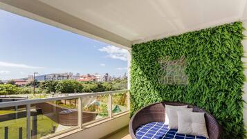 A balcony with a green wall, a wicker chair, and a view of buildings in the distance.