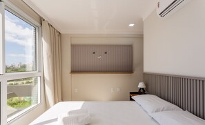 A hotel room with a bed, a window with curtains, a wall-mounted air conditioning unit, and a small bedside table with a lamp. - Full Apartment at Ingleses Beach-sc Gge203 (Florianópolis)