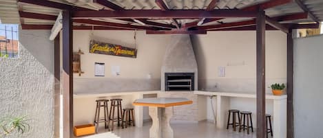 An outdoor kitchen area with a stone table, stools, and a hanging sign.