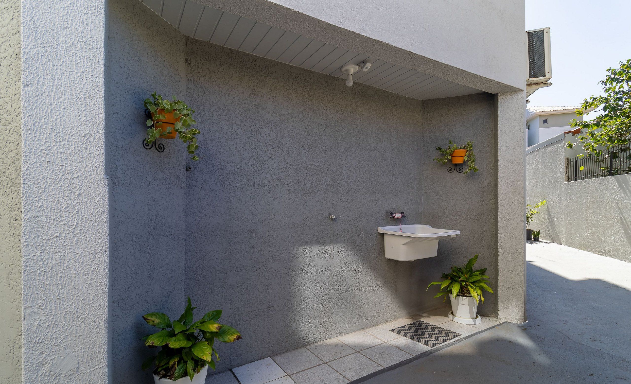 Une salle de bain extérieure moderne avec un lavabo blanc et des plantes en pot.