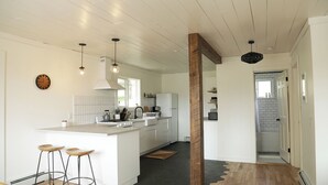 Eine moderne Küche mit weißen Schränken, einer zentralen Kochinsel mit Sitzgelegenheiten, Pendelleuchten und einer Wand in Holzoptik.