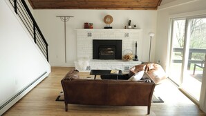 Ein Wohnzimmer mit Kamin aus weißem Backstein, einem braunen Ledersofa und einem Deckenventilator.