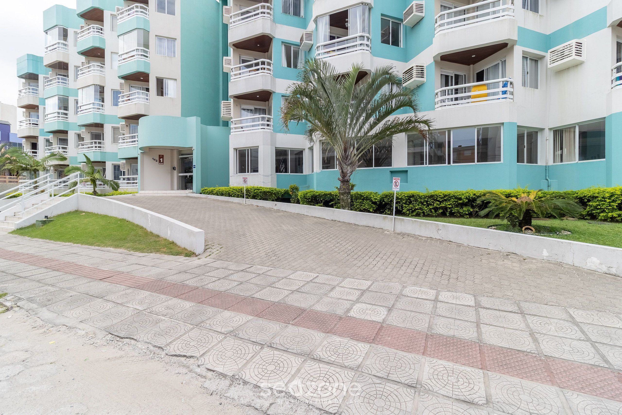 A multi-story residential building with balconies, a palm tree, and a paved walkway.