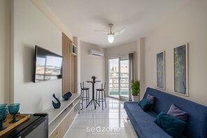 Un salon moderne doté d’un téléviseur à écran plat, d’un ventilateur de plafond, d’un coin repas avec deux chaises et une table, ainsi que d’un canapé avec des coussins.