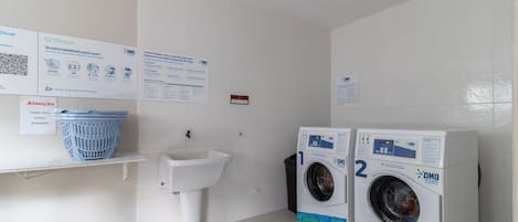 A laundry room with two OMO branded washing machines, a sink, and a blue laundry basket on a shelf.