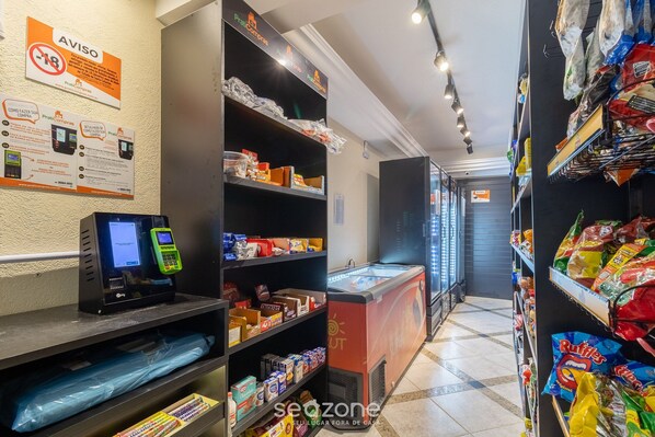 Interior de un supermercado con una máquina de autopago, sección refrigerada y estantes llenos de productos de snacks.
