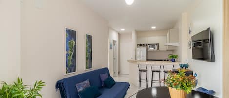 Una sala de estar moderna con sofá, una mesa de comedor y sillas. Cuenta con una zona de cocina con microondas y televisor.