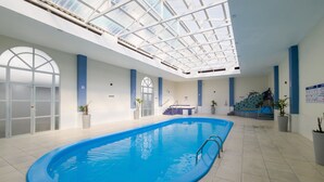 Una piscina interna con soffitto in vetro e vasca idromassaggio, con piante in vaso.