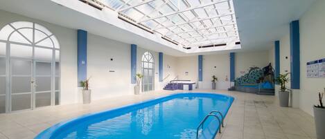 An indoor swimming pool with a skylight ceiling, a hot tub, and potted plants.