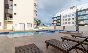 A swimming pool with lounge chairs and a view of modern buildings. - Charming Stay Steps From the Sea Ftm0401 (Florianópolis)