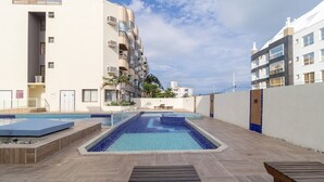 Una piscina sul tetto con un pontile in legno, circondata da edifici con balconi e condizionatori.