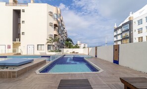 A rooftop swimming pool with a wooden deck, surrounded by buildings with balconies and air conditioning units. - Charming Stay Steps From the Sea Ftm0401 (Florianópolis)