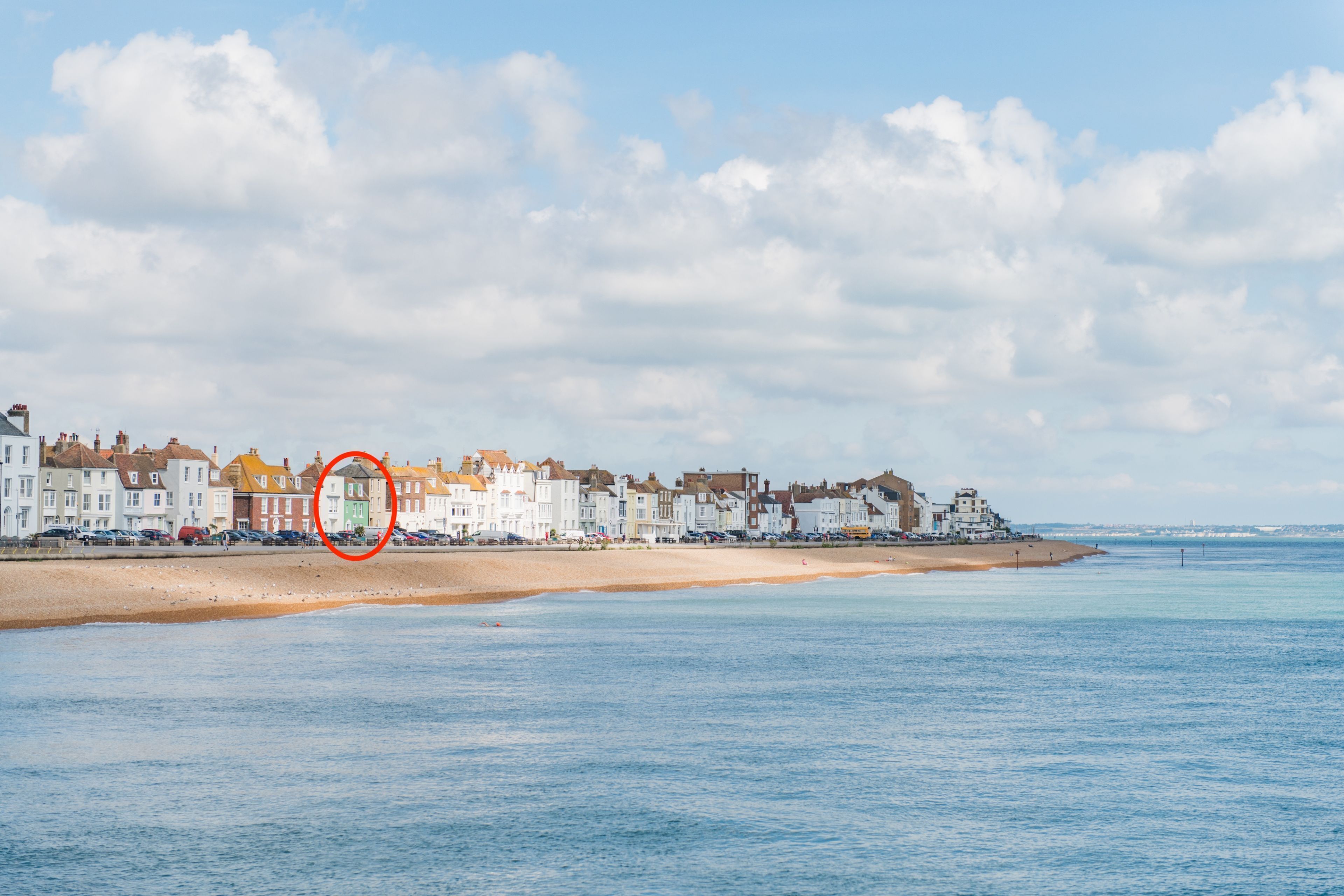 A coastal town with a sandy beach, a row of white buildings, and a clear blue sky.