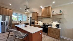 A modern kitchen with wooden cabinets, a large island, stainless steel appliances, and a dining area with wicker chairs. - Peaceful 3-bed, 3 bath house with AC in charming Kingsland (Kingsland)