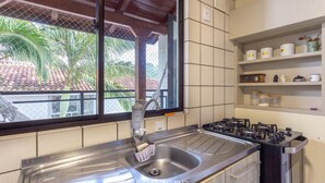 Eine Küche mit einer Edelstahlspüle, einem Gasherd und einem Fenster mit Blick auf Palmen.
