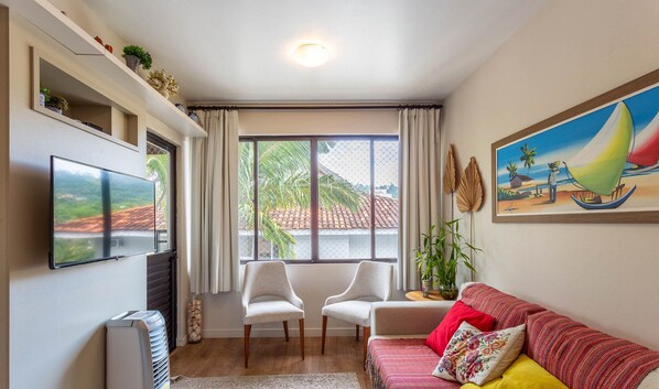A living room with a TV, two chairs, a sofa, a painting, and a window with curtains.