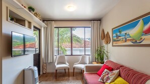 Ein Wohnzimmer mit Fernseher, zwei Sessel, einer Couch, einem Gemälde und einem Fenster mit Vorhängen.