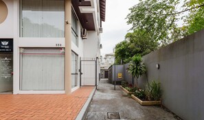 A narrow alleyway with a closed shop on the left and a gated area with plants on the right.