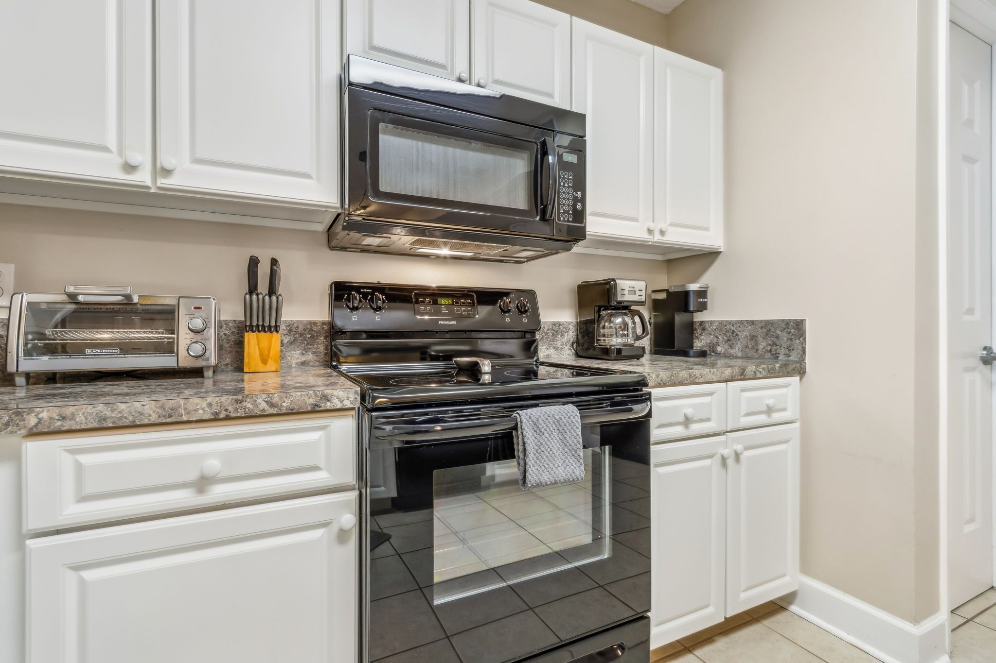 A modern kitchen with white cabinetry, a stainless steel stove, a microwave, a toaster, and a coffee maker.