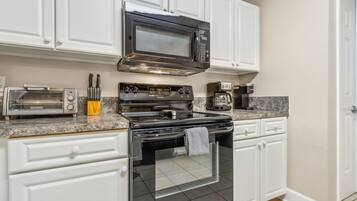 A modern kitchen with white cabinetry, a stainless steel stove, a microwave, a toaster, and a coffee maker.