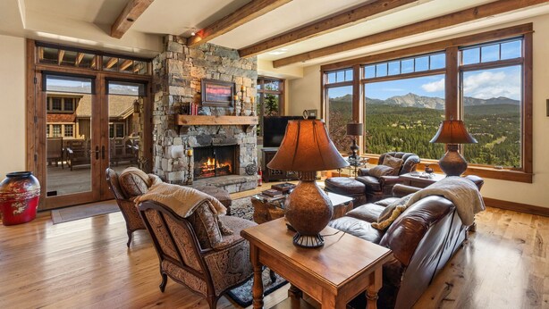 A spacious living room with a stone fireplace, leather furniture, and large windows offering mountain views. - Cowboy Lux - Moonlight Basin Ski In/Out (Big Sky)