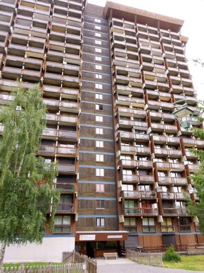 A multi-story residential building with balconies, a wooden facade, and a gated entrance. - 200m from resort center, 12nd floor, view ski slopes, swimming pool, balcony, tv, ski locker, 47m² (Le Corbier)