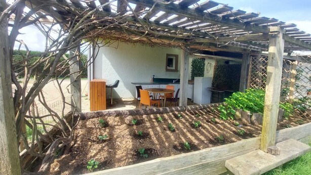 A garden with raised beds, a wooden pergola, and a small outdoor seating area with chairs and a table.