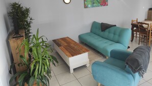 A living room with a sofa, a coffee table, and two chairs. There are two wall-mounted lights and a painting on the wall.