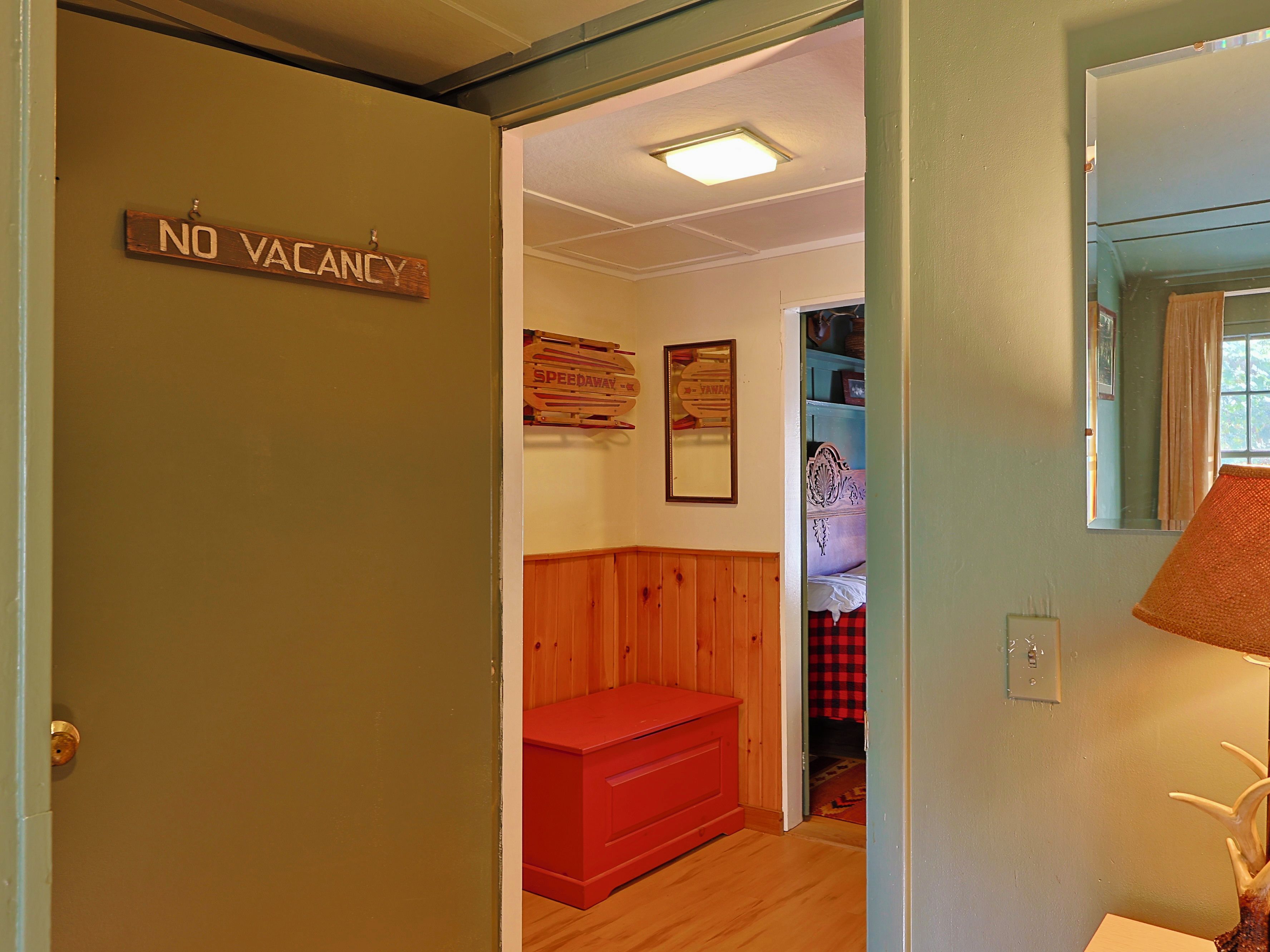 Una habitación con un cartel de 'NO VACANCY', un banco rojo, una pared de madera, un espejo y una lámpara.