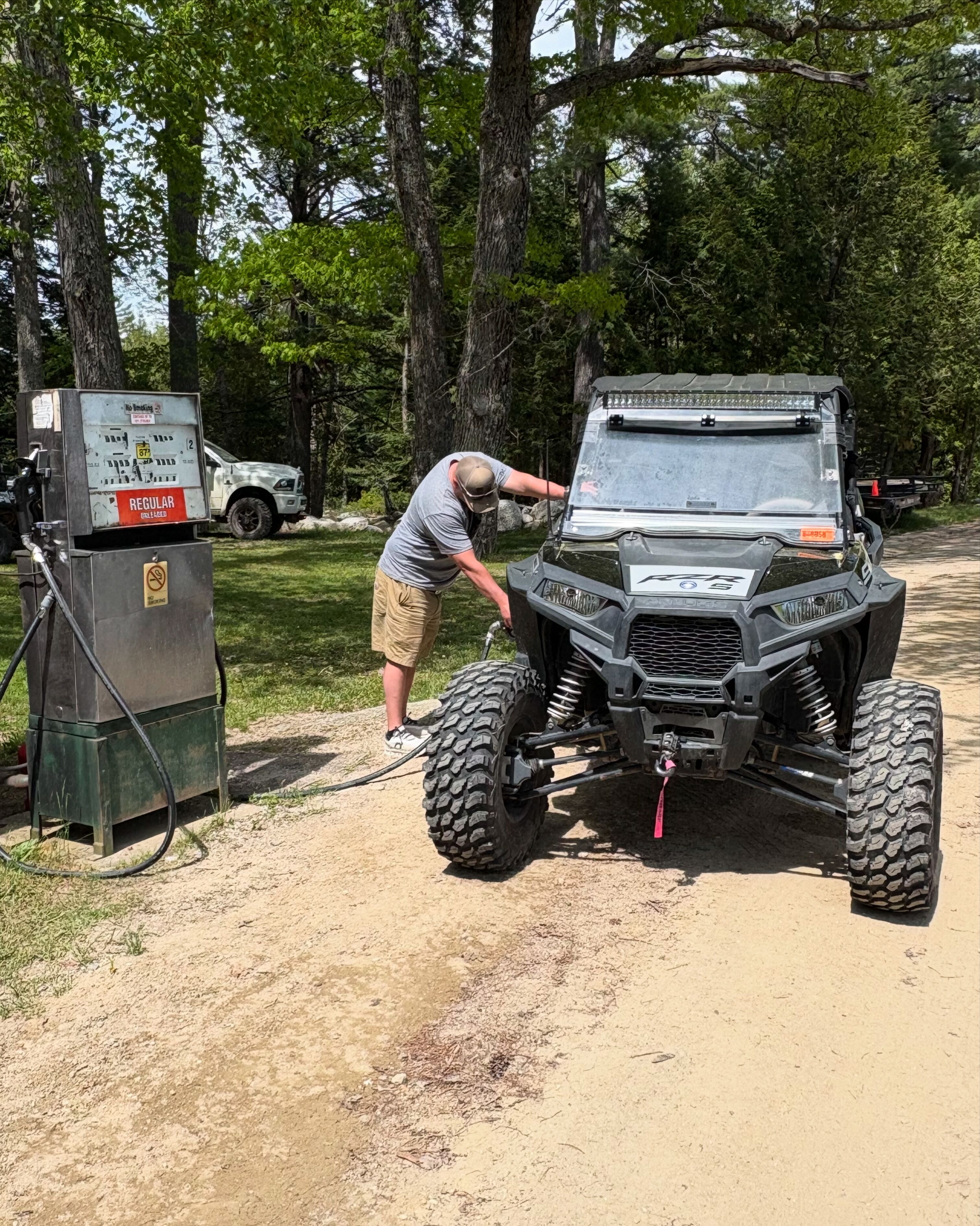 A person working on a vehicle near a fuel pump.