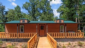 Eine Holzhütte mit einer zentralen Tür, zwei Seitenfenstern und einer Veranda mit Geländern.