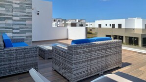 Eine Dachterrasse mit Korbmöbeln, einer Steinwand und modernen Gebäuden im Hintergrund.