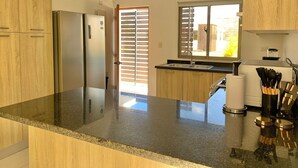 Eine moderne Küche mit Holzausstattung, einem Edelstahlkühlschrank, einer schwarzen Arbeitsplatte, einem Fenster mit Jalousien und einer Spüle mit Besteck.