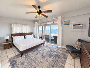 A bedroom with a bed, a ceiling fan, a view to the outside, and a balcony with chairs.