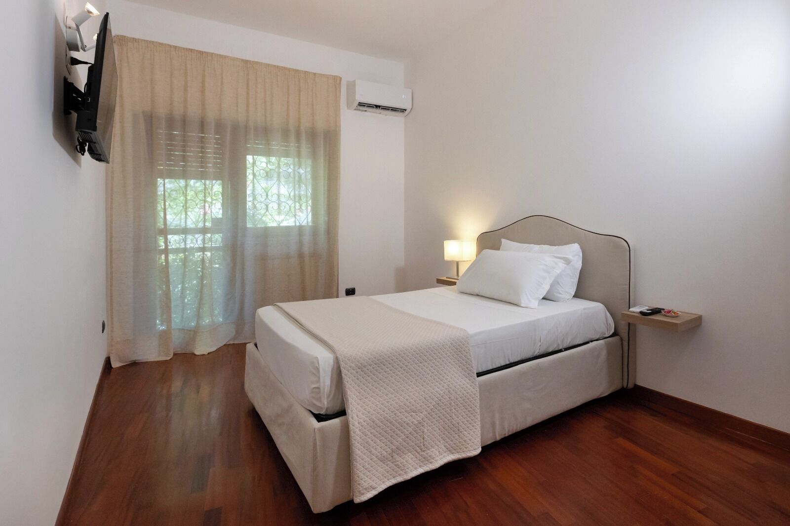 Un dormitorio ordenado con cama, mesita de noche y televisor montado en la pared.