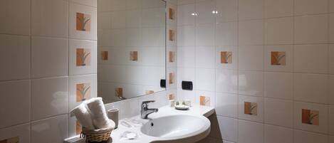 A bathroom with white tiles, a large mirror, a white sink, and a towel rack.