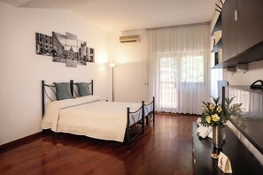 A bedroom with a bed, a bedside table with a vase of flowers, a mirror, and a window with sheer curtains. - Residenza in Vaticano Roma (Rome)