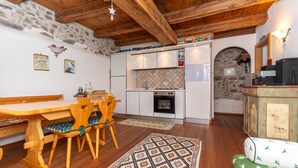 A cozy kitchen with wooden beams, a stone wall, and a dining area with a table and chairs. - Tamion House (Vigo di Fassa)