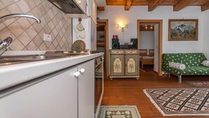 A kitchen with a sink, stove, and cabinets, a dining area with a table and chairs, and a green sofa with patterned cushions. - Tamion House (Vigo di Fassa)