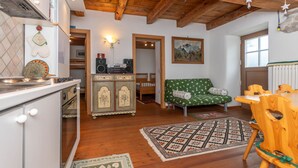 A cozy kitchen with wooden beams, a green patterned sofa, and a dining area with wooden chairs. - Tamion House (Vigo di Fassa)