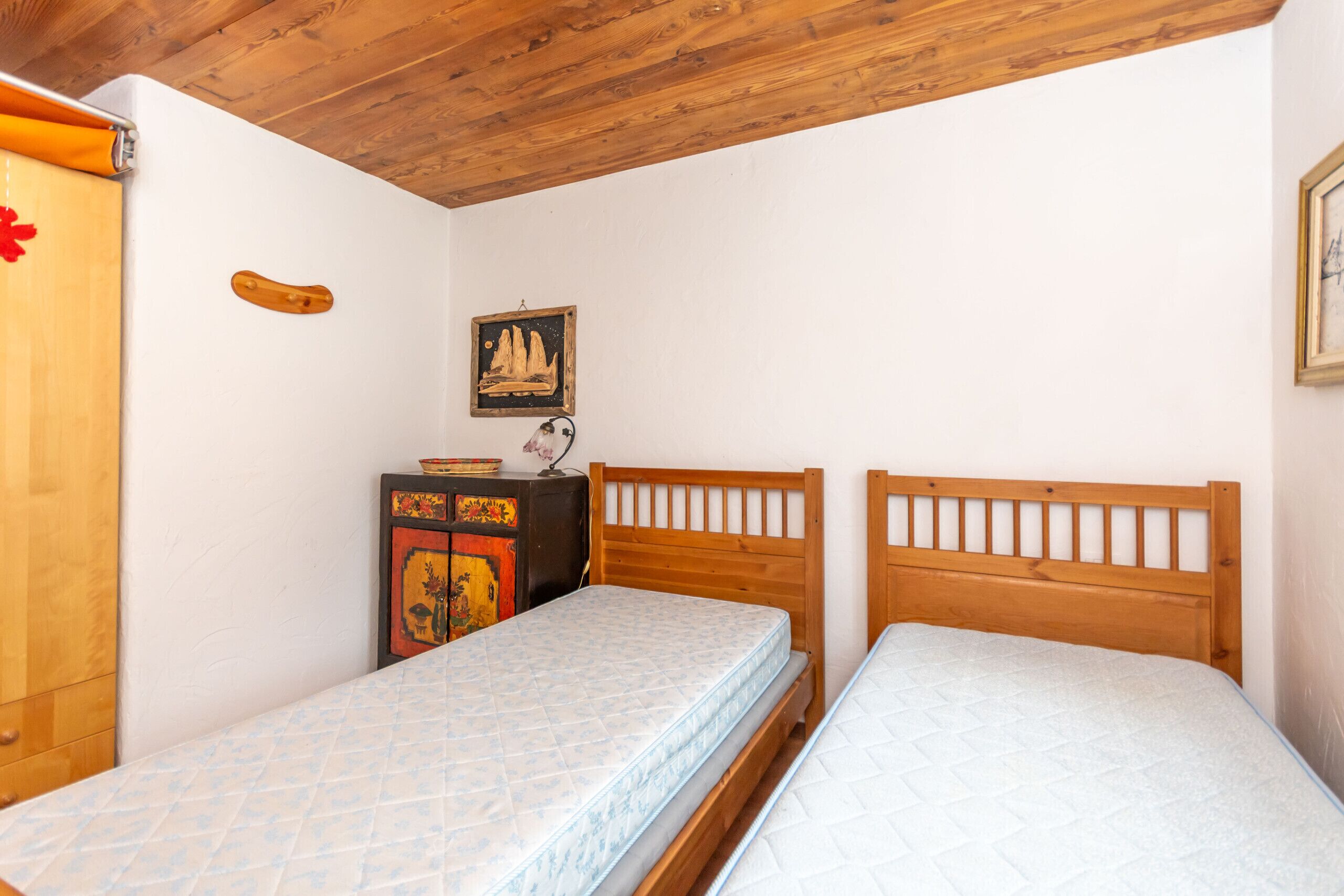 Une petite chambre à coucher avec deux lits en bois, un plafond en bois et une petite armoire sur laquelle est posé un objet décoratif.