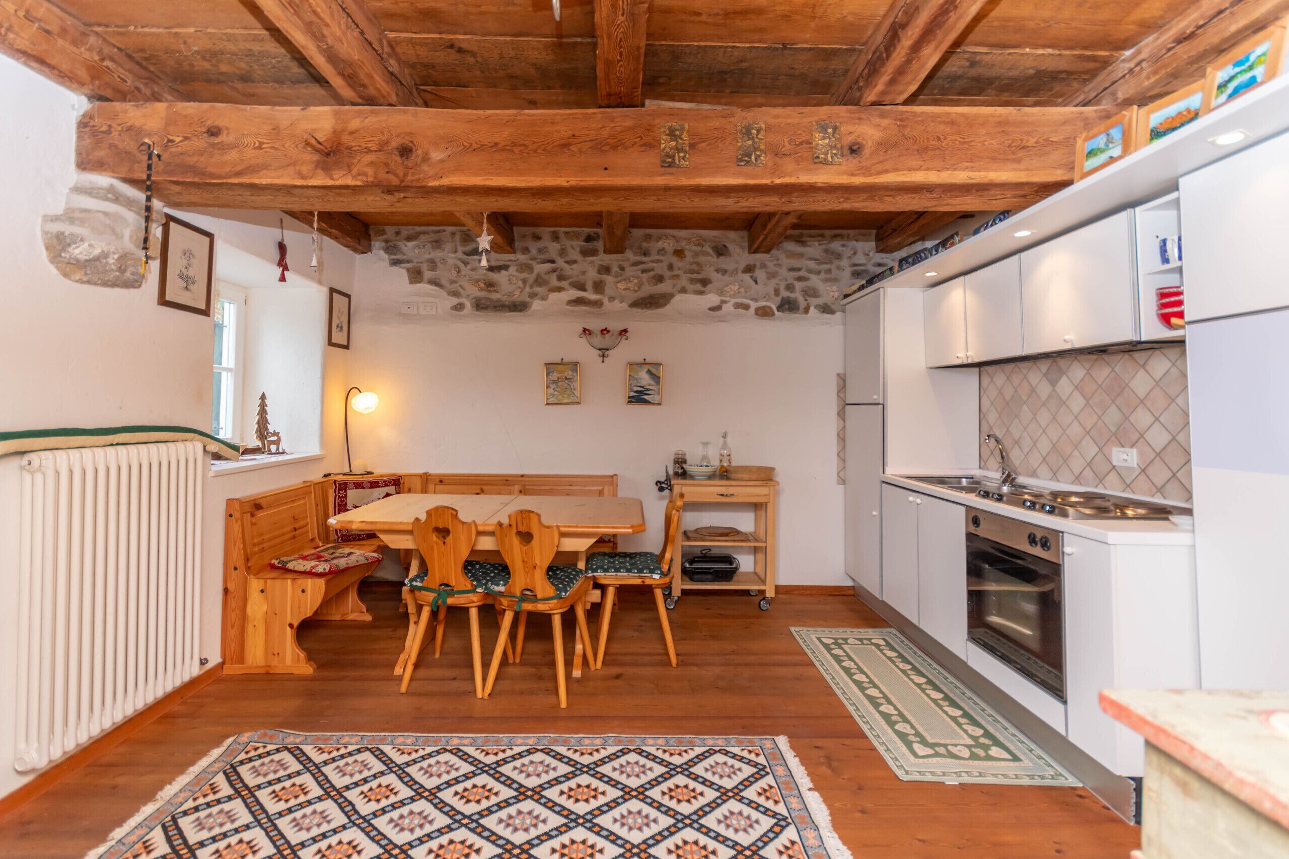 Una cocina rústica con vigas de madera, pared de piedra y zona de comedor con banco y sillas.
