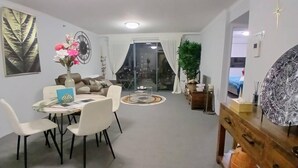 Un salon moderne comprenant un coin repas, une grande fenêtre avec des rideaux, une plante et un élément décoratif mural.