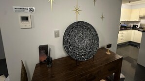 Une cuisine moderne avec des meubles blancs, une table à manger en bois, un élément décoratif mural et un panneau indiquant «Il est interdit de fumer».