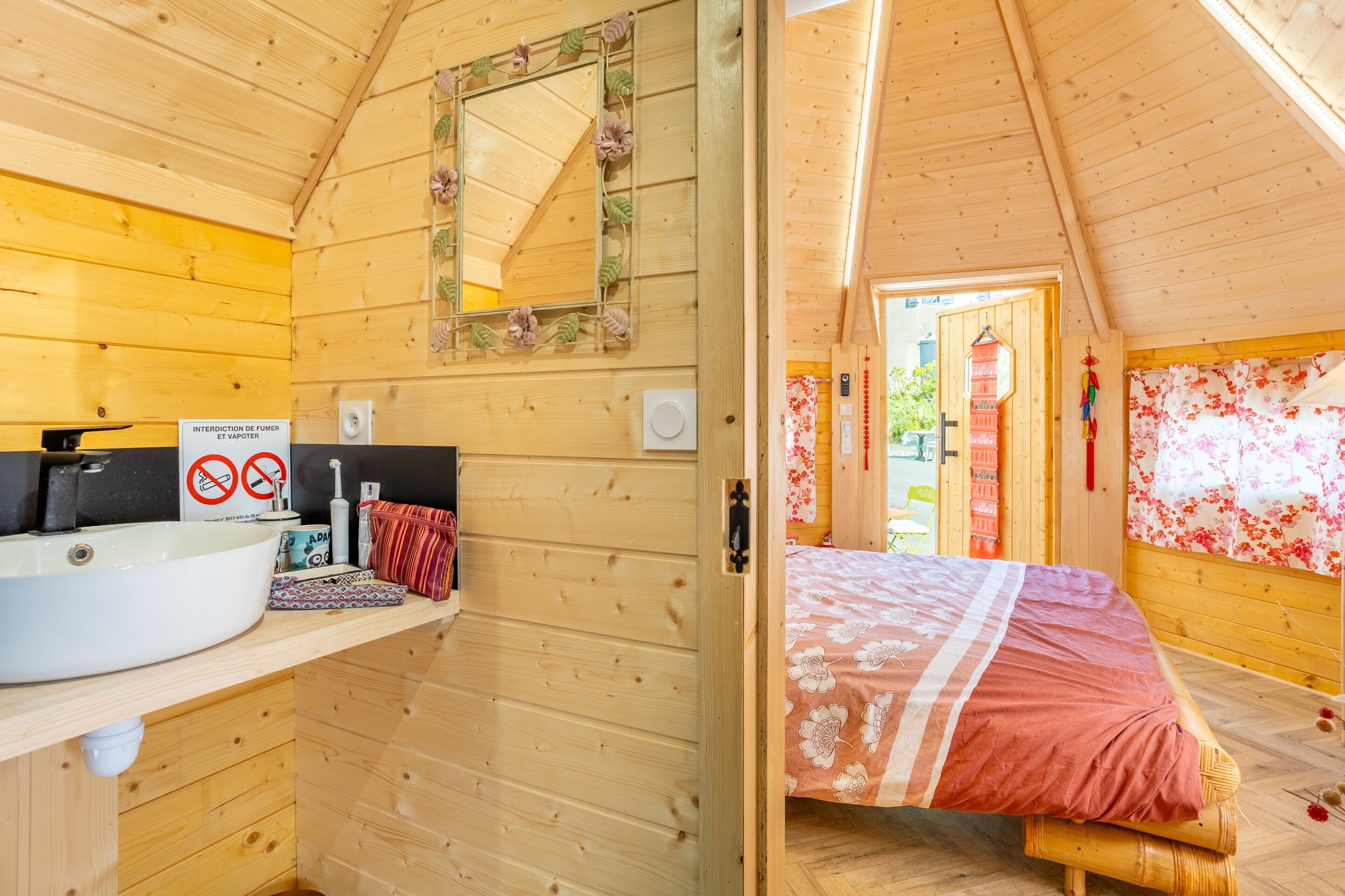 Een houten blokhut van binnen met een badkamer, een bed en een spiegel.