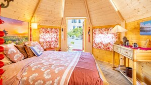 Ein Zimmer mit einem Bett, Holzwänden, einem Schreibtisch und Blick ins Freie.
